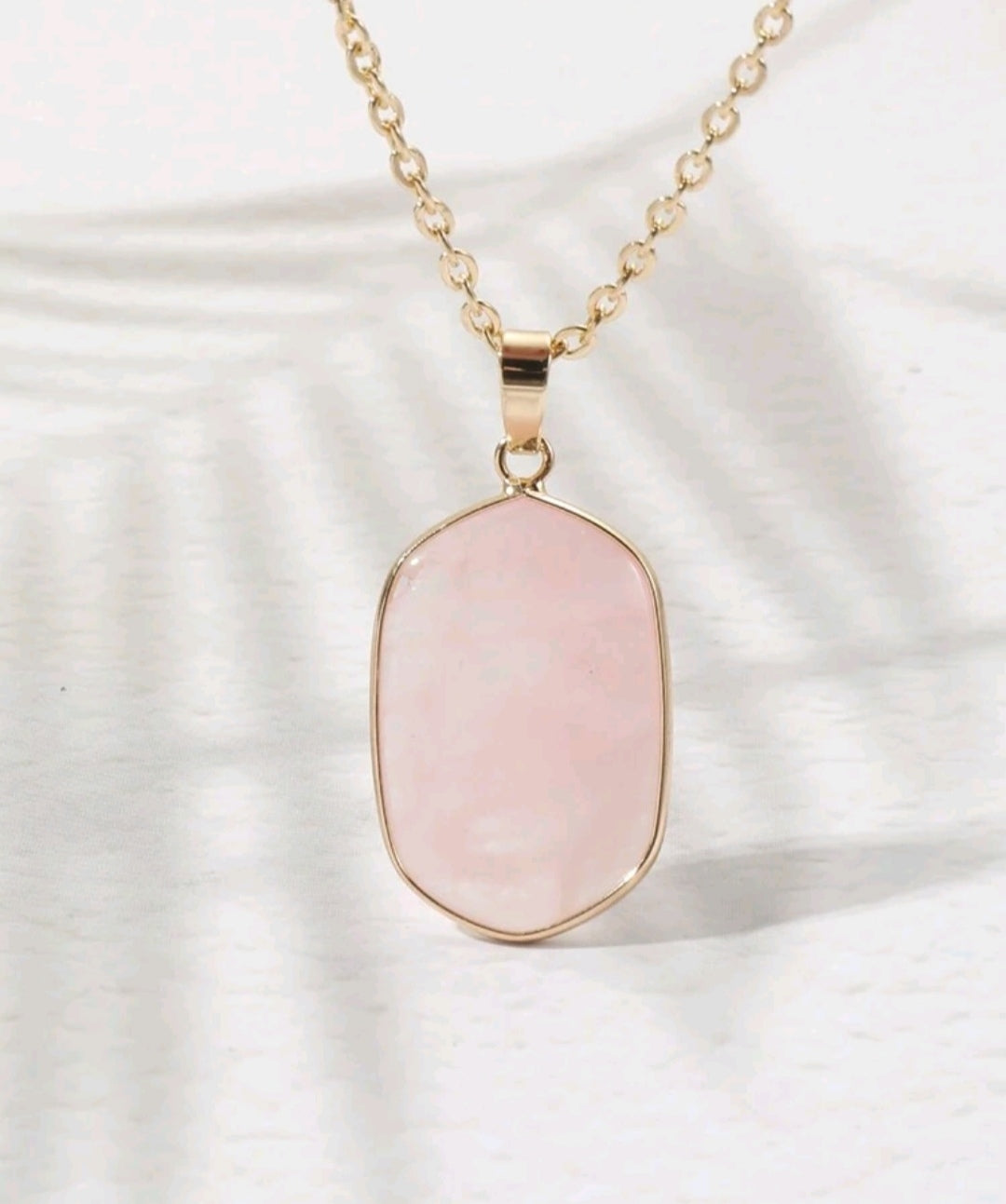colgante de cuarzo rosa pulido con baño dorado sobre fondo neutro