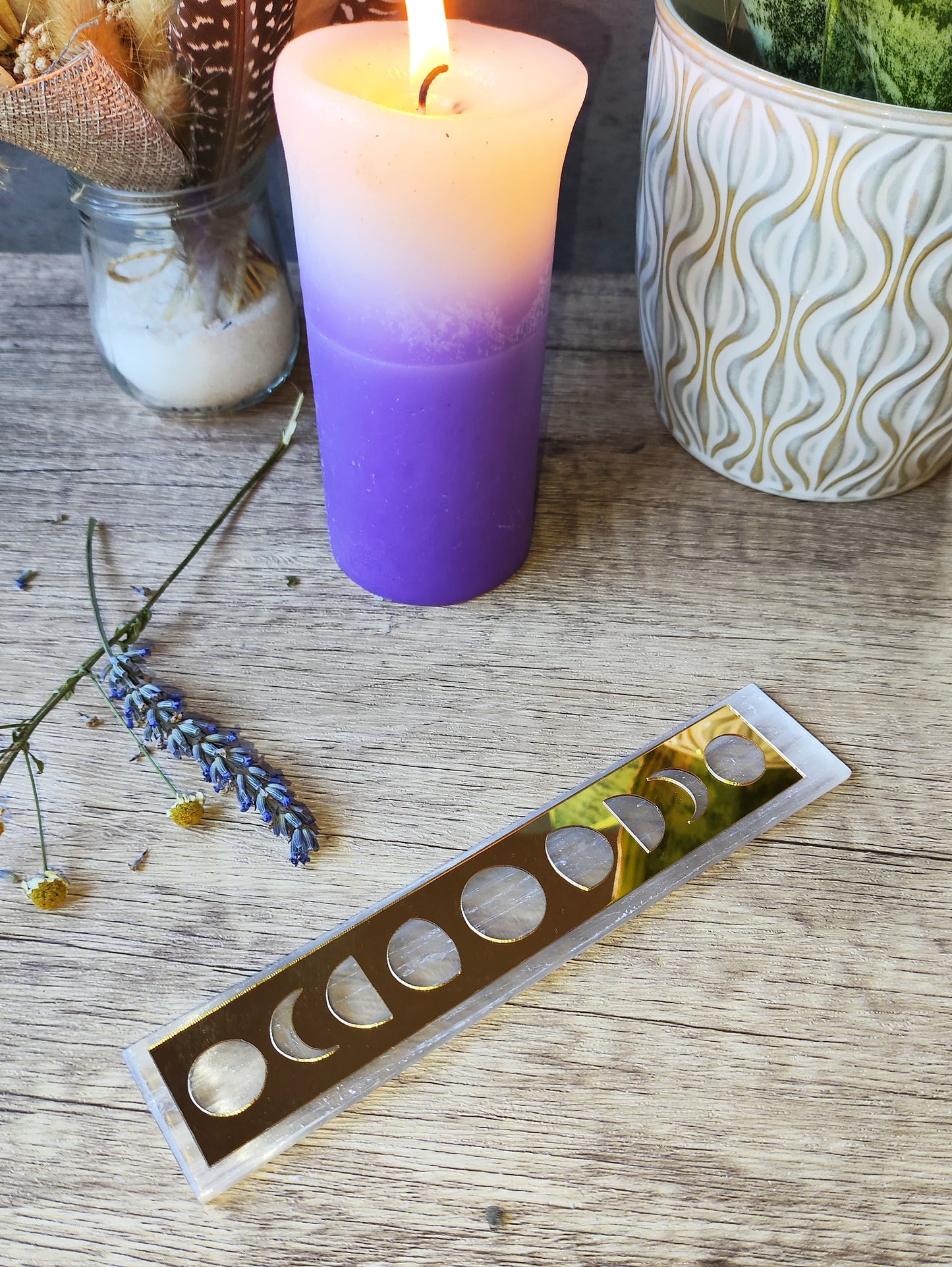 placa rectangular de selenita con fases lunares doradas junto a vela encendida, lavanda y decoración esotérica.