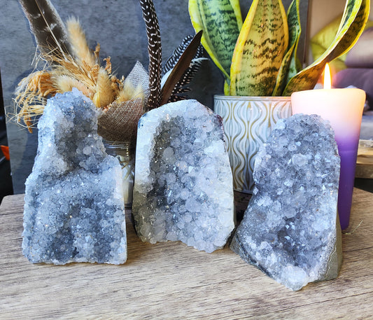 Drusas de amatista clara con brillo natural, acompañadas de decoración esotérica y vela violeta.

