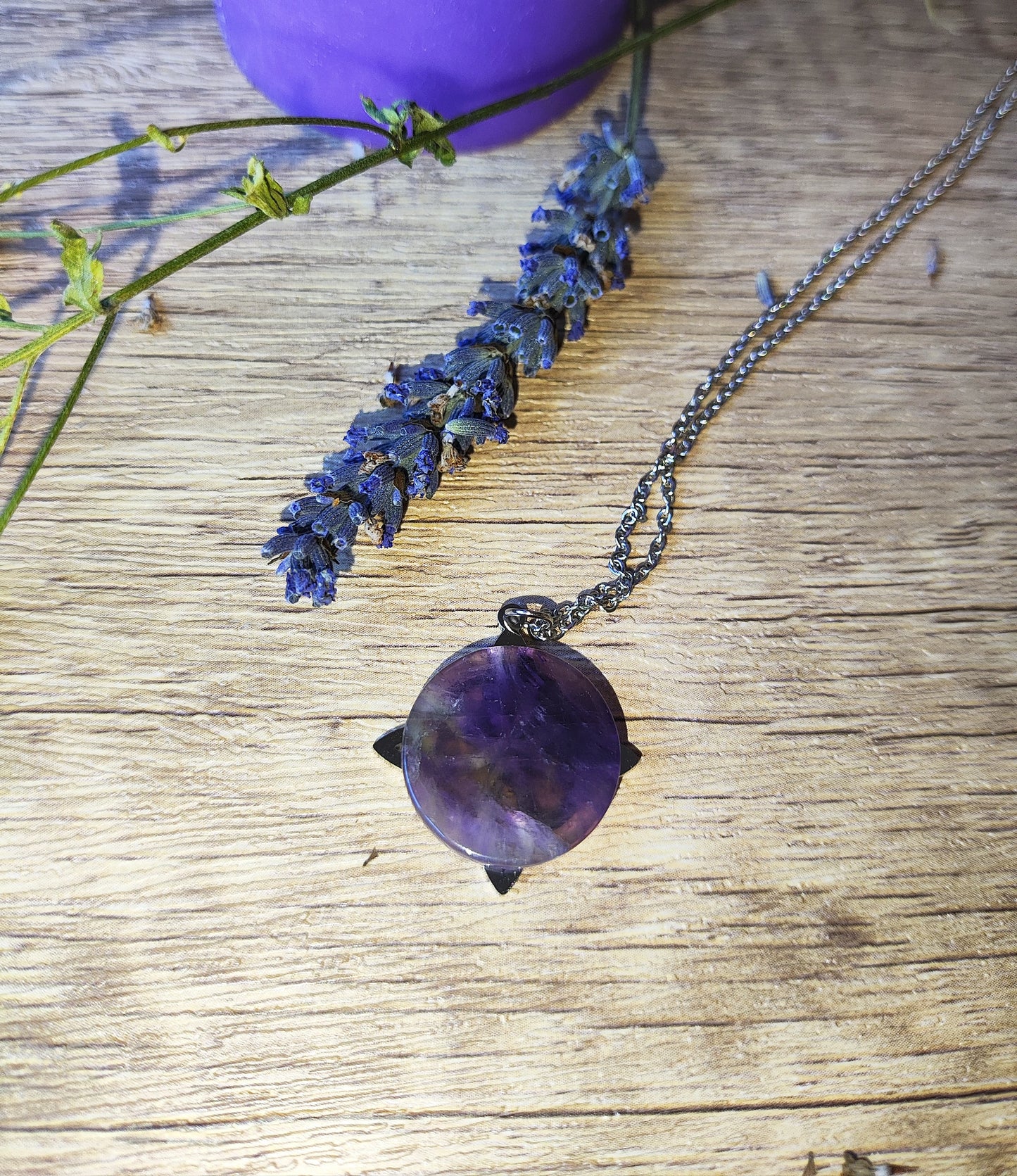 Colgante de amatista circular con cadena de acero, presentado en estilo natural y mágico sobre fondo rústico.