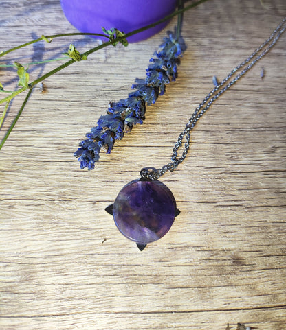 Colgante de amatista circular con cadena de acero, presentado en estilo natural y mágico sobre fondo rústico.
