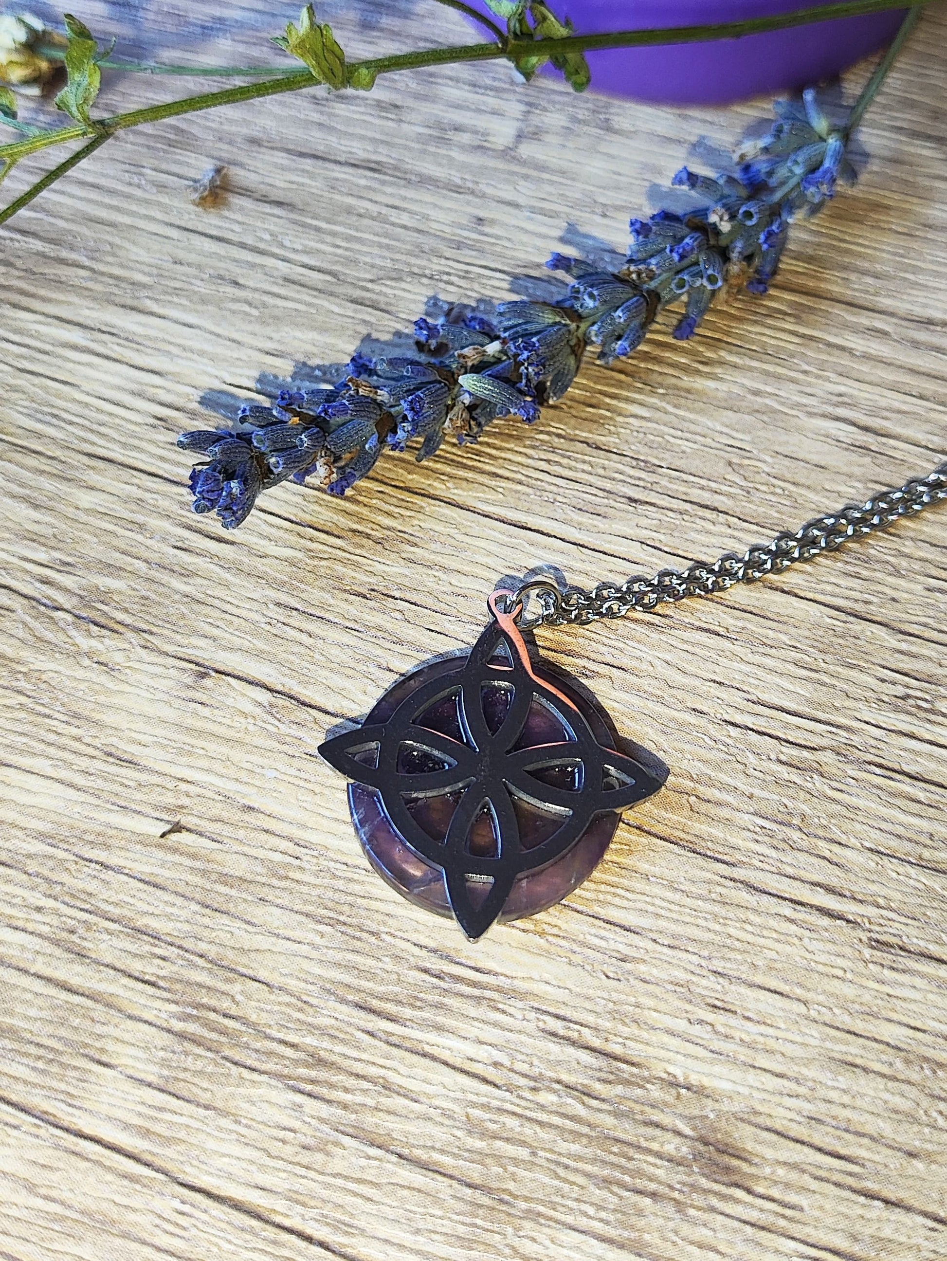 Colgante nudo de brujas con amatista sobre fondo de madera, junto a lavanda seca y flores, joya esotérica con simbología protectora.