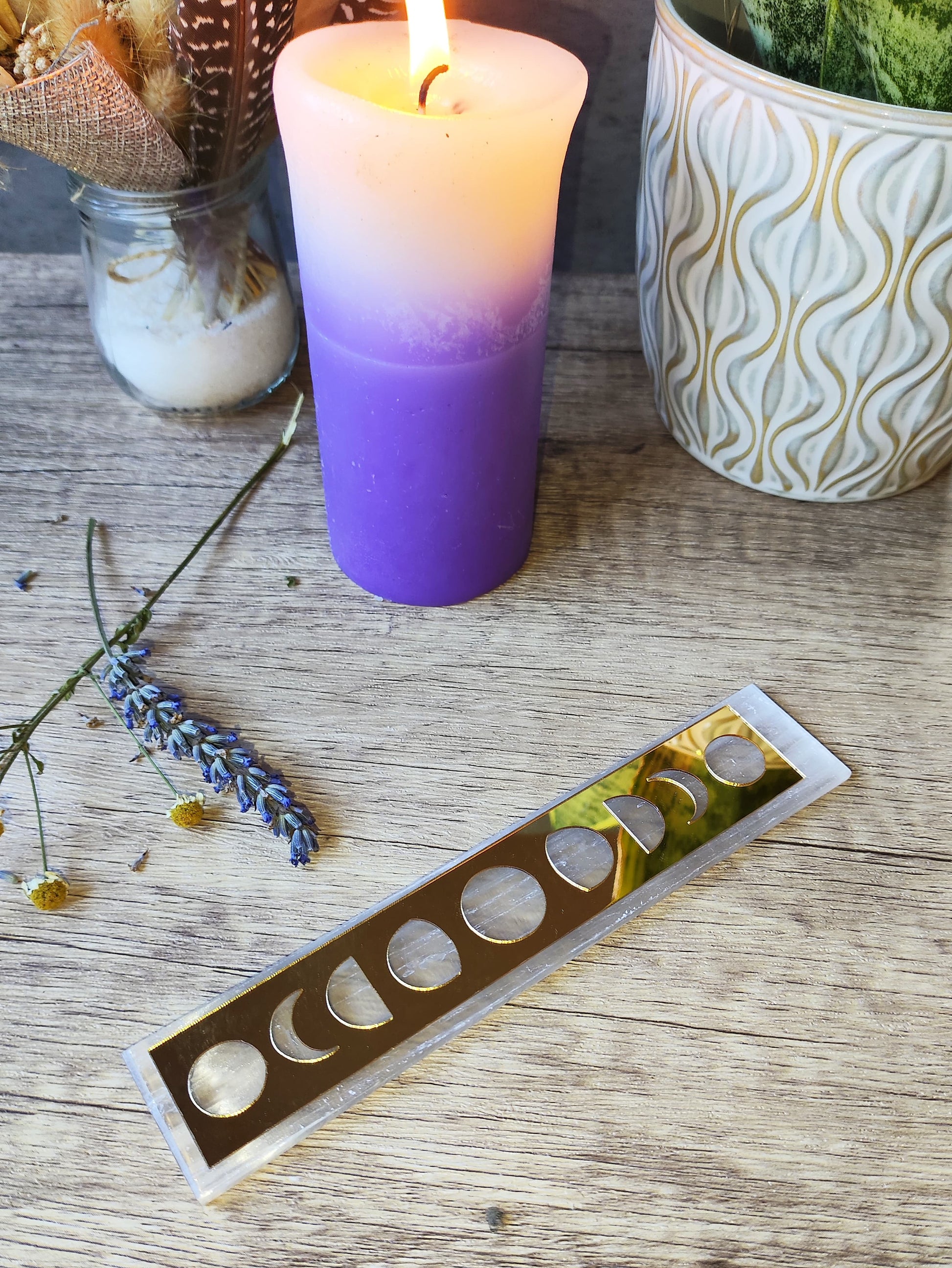 placa rectangular de selenita con fases lunares doradas junto a vela encendida, lavanda y decoración esotérica.